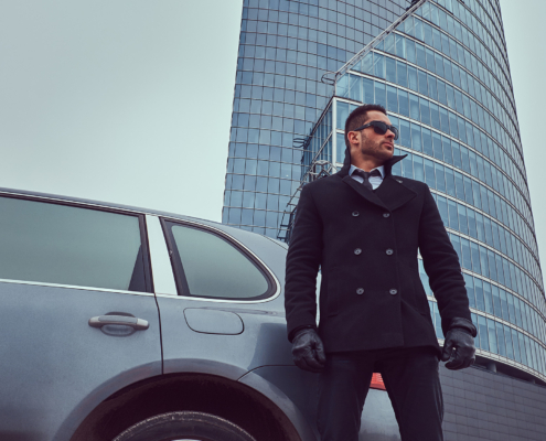 Worm's eye view of a man in a suit and sunglasses standing outside a car